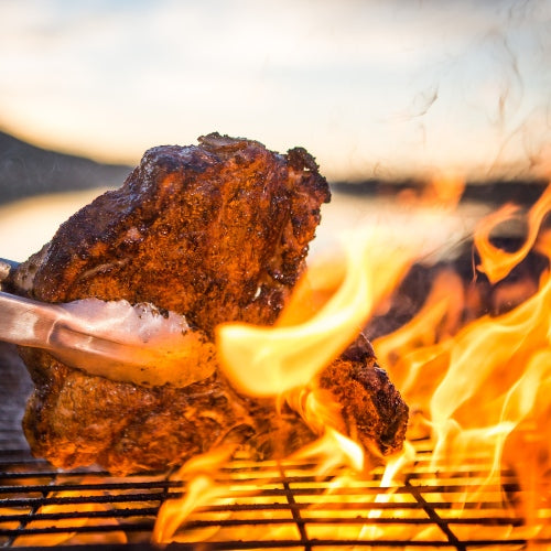 Beef cooking on the grill with flames.